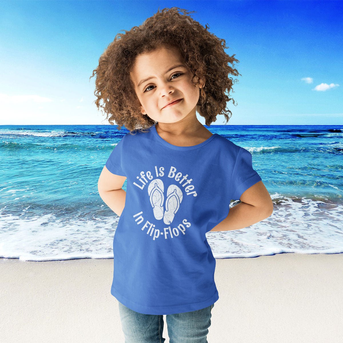 Child wearing a blue t-shirt with 'Life is Better in Flip-Flops' text on a beach.