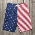 Men's American flag pattern board shorts on a rustic wood deck