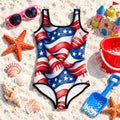 One-piece swimsuit with American flag print on a sandy background with beach elements.