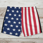 Men's American flag patterned swim shorts on a rustic wood background.
