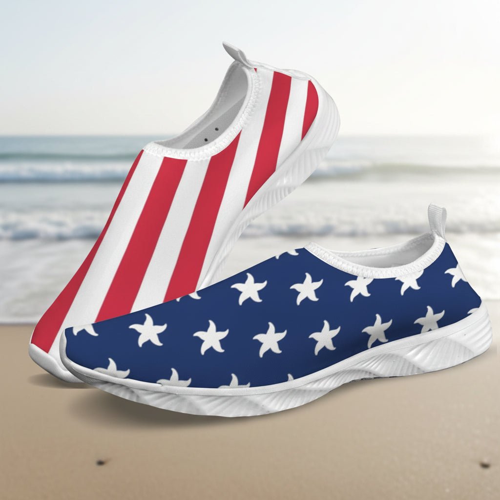 A pair of slip-on water shoes with an American flag theme, featuring red and white stripes on one shoe and white stars on a navy blue background on the other, set against a faded beach background.