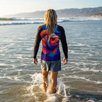 Surfer dude wearing a colorful fish-themed shirt walking in ocean waves with mountains in the background near Ventura Beach