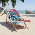 A beach chair on a sandy beach with a colorful printed blanket featuring a vintage blue truck and sunset stripes.