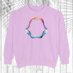 A light purple crewneck sweatshirt featuring a colorful graphic of an open mouth with sharp teeth on the chest, displayed against a white wood plank background.