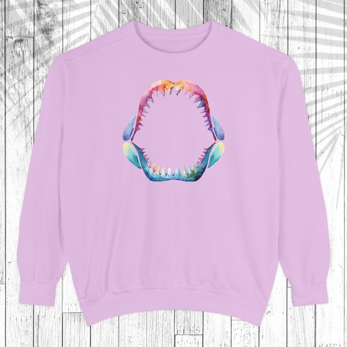 A light purple crewneck sweatshirt featuring a colorful graphic of an open mouth with sharp teeth on the chest, displayed against a white wood plank background.