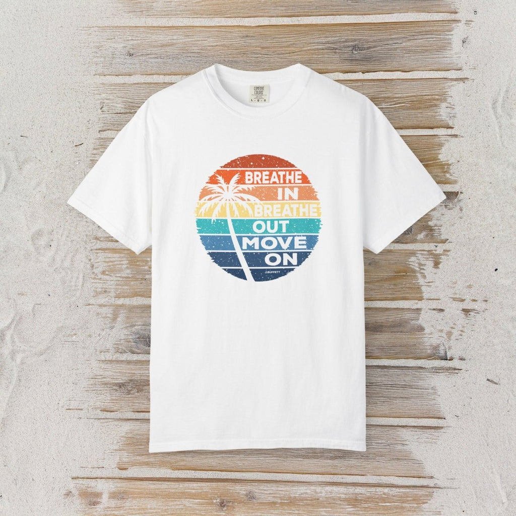A white short-sleeve crewneck t-shirt with a circular retro graphic on the chest. The graphic features a sunset gradient in orange, yellow, and blue with a palm tree silhouette and the text 'BREATHE IN BREATHE OUT MOVE ON'.