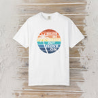 A white short-sleeve crewneck t-shirt with a circular retro graphic on the chest. The graphic features a sunset gradient in orange, yellow, and blue with a palm tree silhouette and the text 'BREATHE IN BREATHE OUT MOVE ON'.