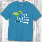 Blue Margarita Party Tee with a graphic of a green cocktail and text 'She's The One To Blame' on a wooden surface.