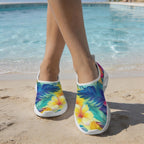 A person standing on a sandy beach with a swimming pool in the background, wearing slip-on Women's Water Shoes with a colorful tropical floral and leaf print.