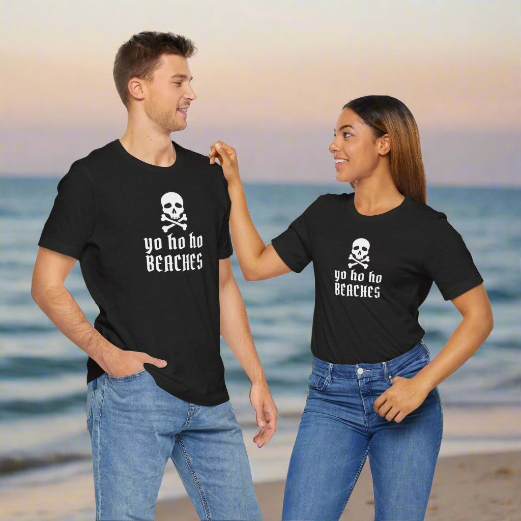Two people wearing black t-shirts with a skull and crossbones design and text on a beach.