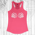 A bright pink racerback tank top with a white graphic of two skeletal hands forming a heart shape on the chest, displayed flat against a white wood plank background with a palm leaf overlay.