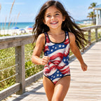little girl in One-piece swimsuit with American flag design on a beachside boardwalk.