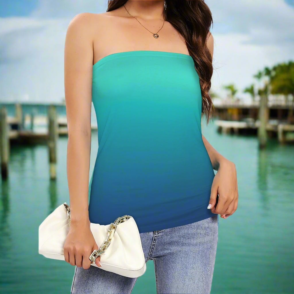 Woman wearing a aqua to navy  strapless top and blue jeans, holding a white clutch while standing on a pier in a Key West Marina
