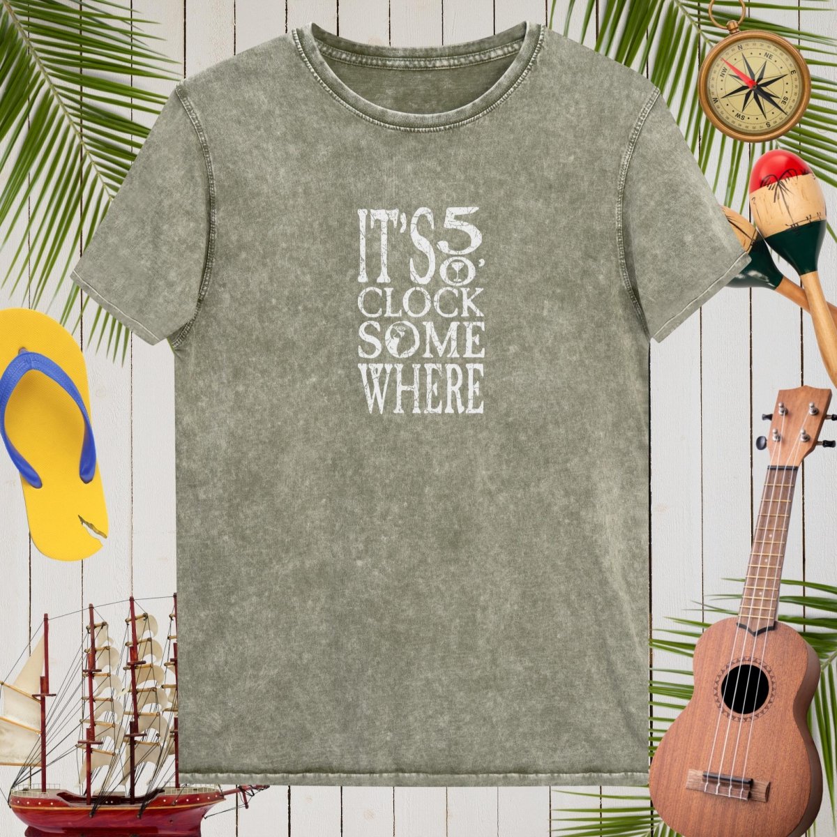 Gray t-shirt with 'It's 5 o'clock somewhere' text, surrounded by tropical-themed items on a wooden background.