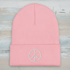 A light pink ribbed knit beanie hat with a folded cuff, featuring a white embroidered peace sign on the front.