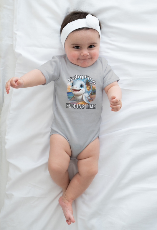 Baby wearing a gray onesie with a cartoon baby shark and text, lying on a white blanket.