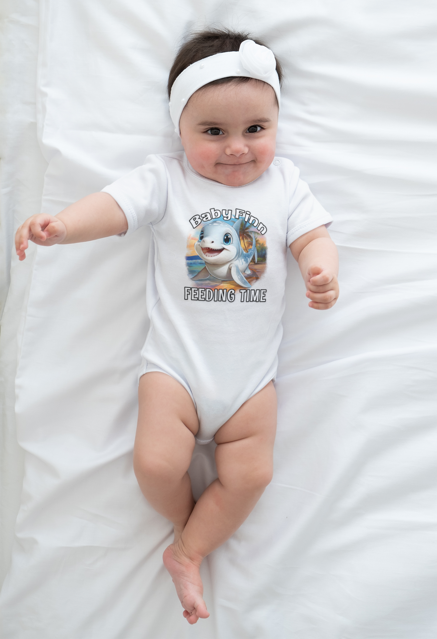 Baby wearing a white onesie with a graphic baby shark design on a white blanket