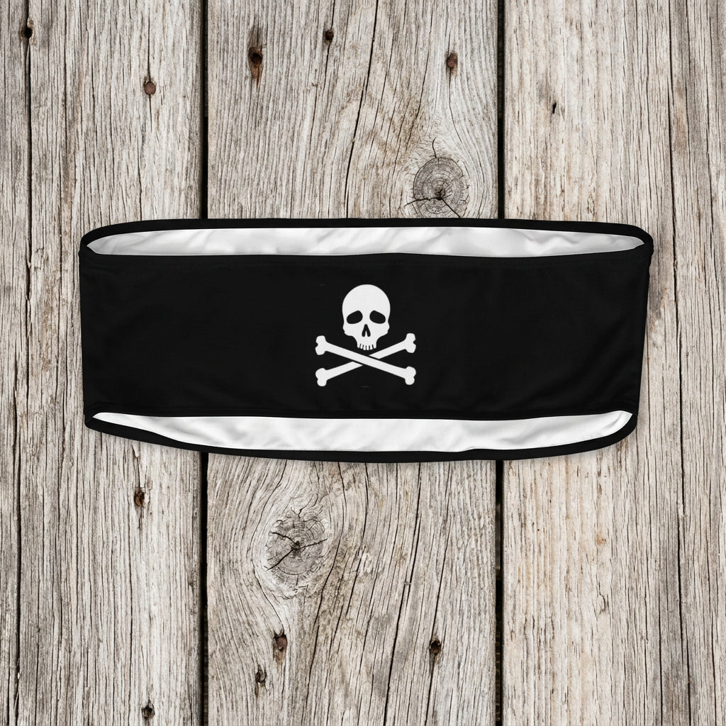 A black athletic headband featuring a white skull and crossbones graphic in the center, displayed against a faded nautical wood background