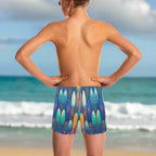 Teen dude wearing colorful surfboard-patterned swim shorts standing on Waikiki Beach looking out over the Pacific