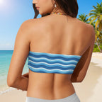 Woman wearing a blue and white striped bikini top on a beach with palm trees and clear blue sky.