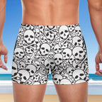 Person wearing black and white skull-patterned swim shorts with a beach background