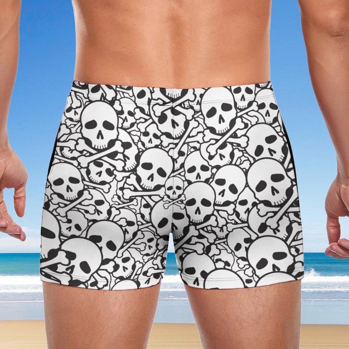 Person wearing black and white skull-patterned swim shorts with a beach background