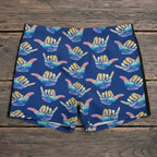 Blue swim shorts with colorful hang loose shaka signs pattern on a beach.