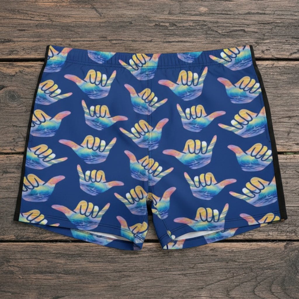 Blue swim shorts with colorful hang loose shaka signs pattern on a beach.
