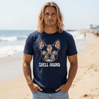 A man with long blonde hair stands on a sandy beach wearing a navy blue Beach Doggy t-shirt with a colorful French Bulldog graphic and the text 'SHELL HOUND'.