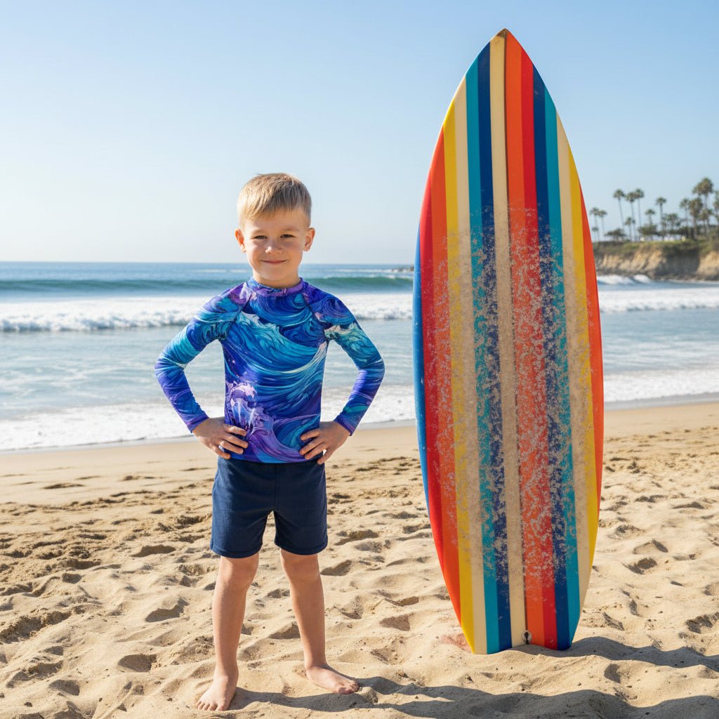 Child wearing a colorful wave-patterned shirt standing next to colorful striped surfboard on La Jolla Beach