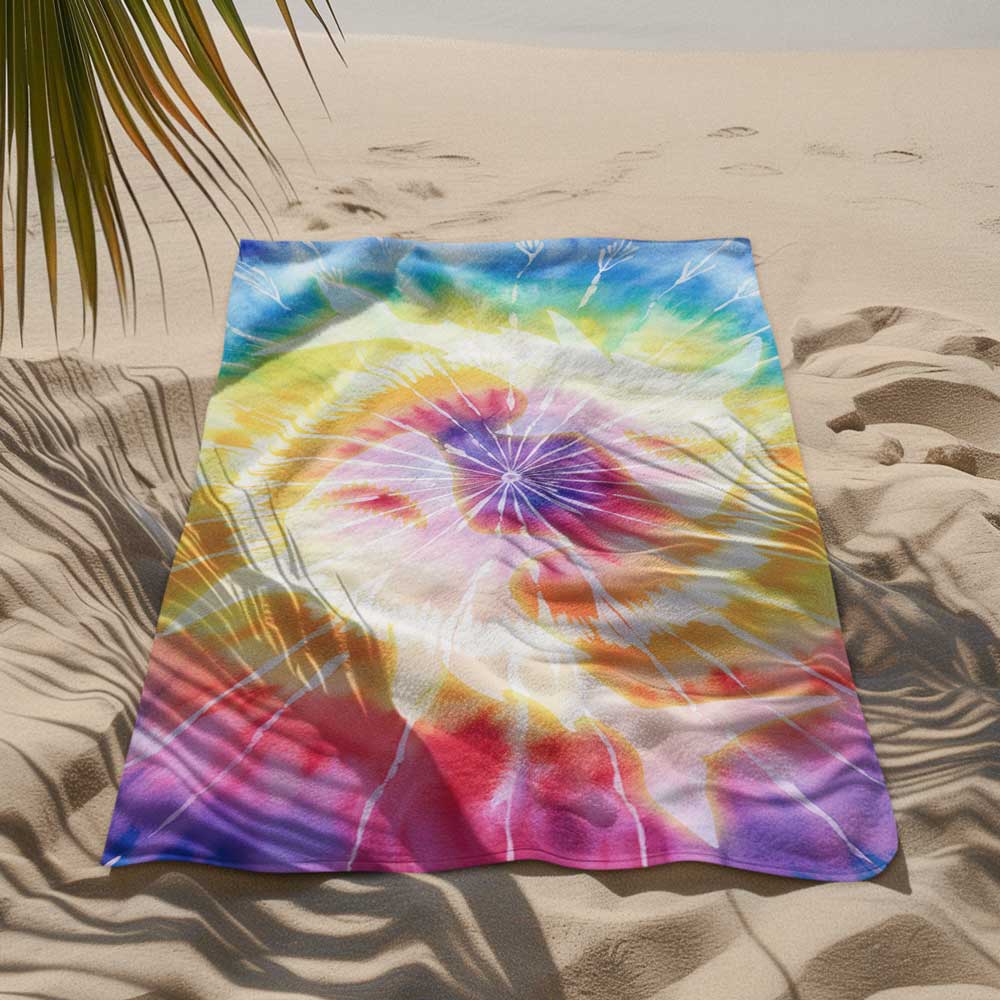 Tie-Dye Beach towel with circling sharks knocked out of the pattern. lying in the sand at the beach
