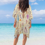 Person wearing a shell-patterned cover-up on a beach with clear blue water and sky.