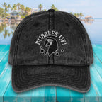 Black cap with 'Bubbles Up!' text and graphic on a teal surface with a pool and palm trees in the background