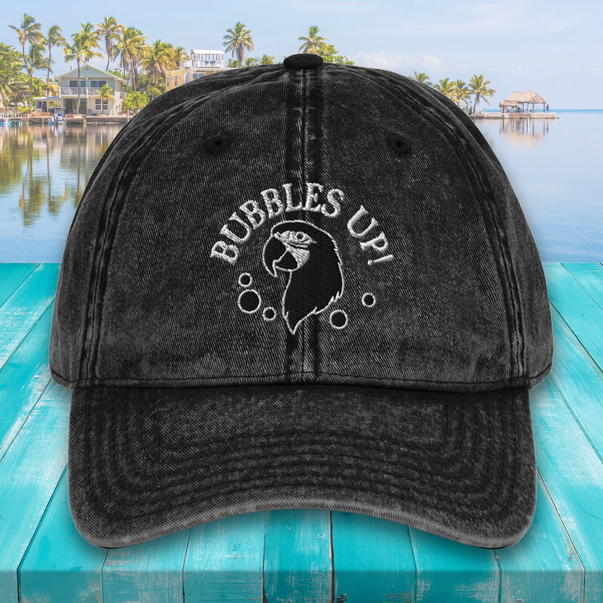Black cap with 'Bubbles Up!' text and graphic on a teal surface with a pool and palm trees in the background