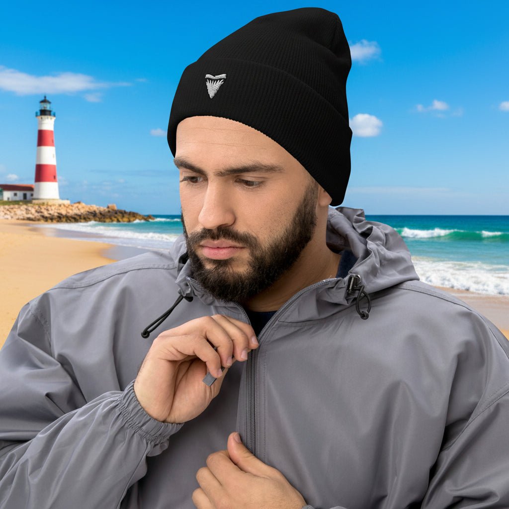 Man wearing a black shark tooth beanie and gray jacket on a northern shore beach near a lighthouse