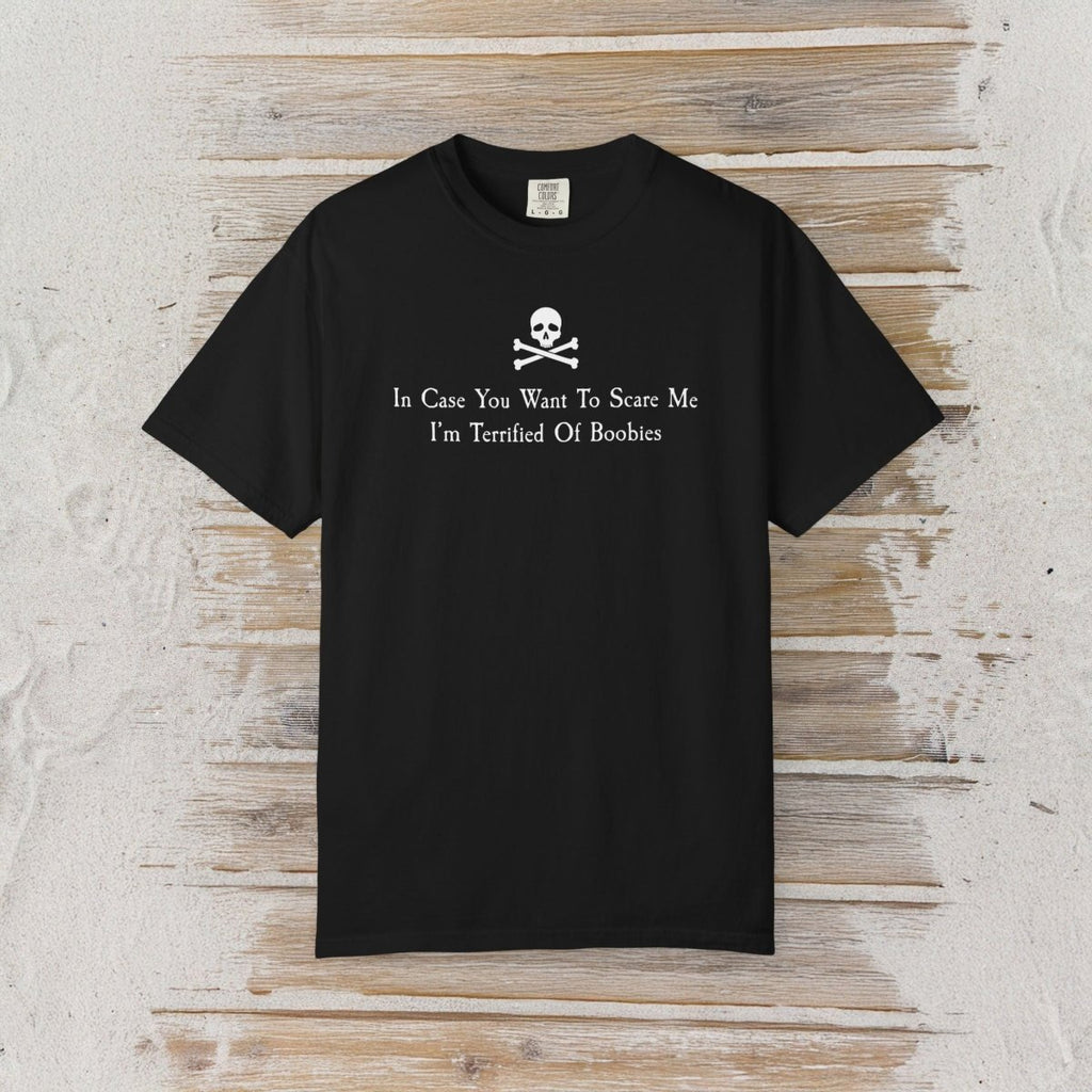 A black short-sleeve crewneck t-shirt with a white skull and crossbones graphic and the text 'In Case You Want To Scare Me I'm Terrified Of Boobies' printed on the chest, displayed flat against a rustic whitewashed wood background.