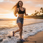 beautiful woman with long blond hair running through the waves wearing blue jean shorts, a black bikini top, and lightweight running shoes with a vibrant purple, pink, and blue tribal pattern pattern and black trim. on black sand beach on the Big Island in Hawaii