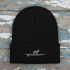 A black ribbed knit beanie hat with a folded cuff, featuring a small gray embroidered graphic of a frenchie bulldog standing on a surfboard on the front.