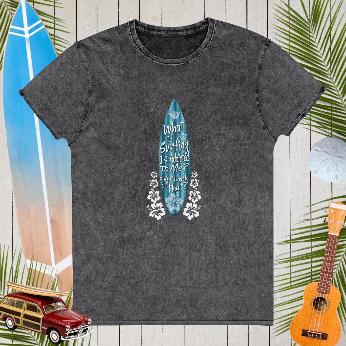 Gray t-shirt with a blue surfboard design and text on a wooden background with tropical elements.