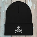 A black ribbed knit beanie hat with a folded cuff, featuring an embroidered silver skull and crossbones on the front, set against a plain white background.