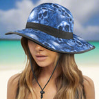 Blue pirate skull-patterned sun hat with black band worn by a model on a caribbean beach background