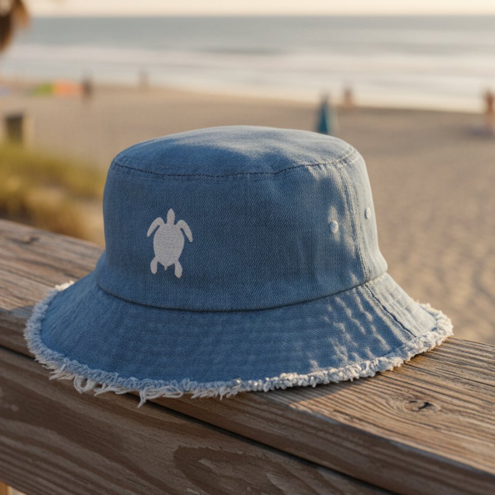 Blue denim bucket hat with sea turtle embroidery on a beachside boardwalk