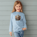 Child wearing a light blue sweatshirt with laughing tiki bongo design against a wooden nautical wall.