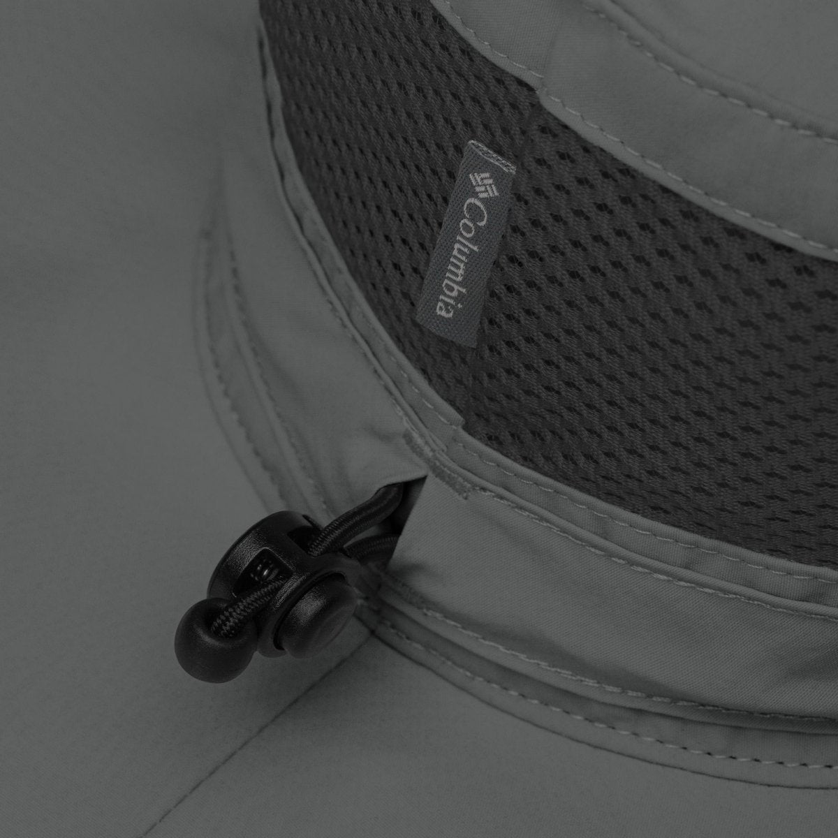 Close-up of Columbia logo on a gray booney hat with adjustable pulltab.