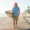 Surfer dude wearing colorful geometric patterned shorts on a beachside boardwalk with his surfboard