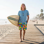 Surfer dude wearing colorful geometric patterned shorts on a beachside boardwalk with his surfboard