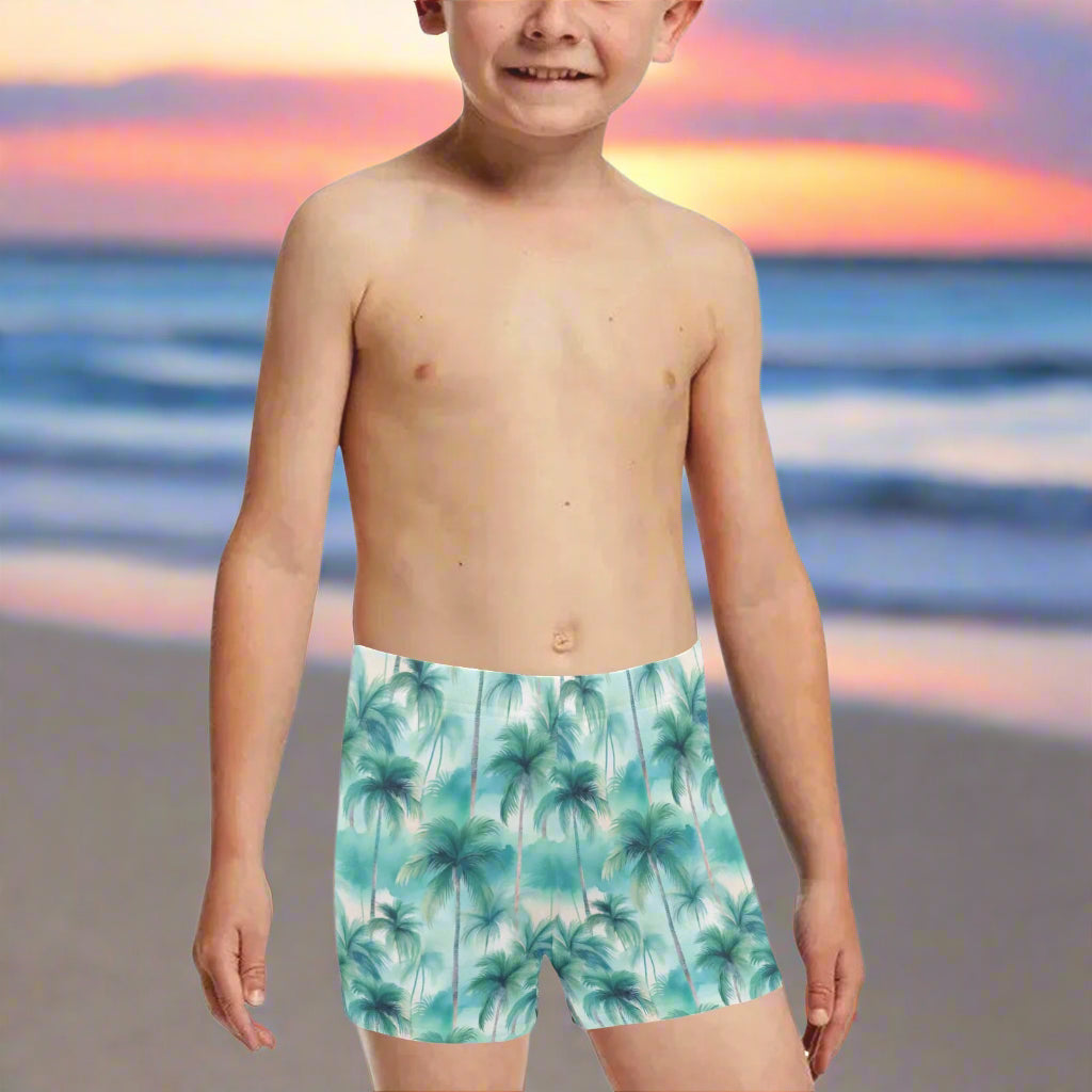 Boy wearing palm tree patterned swim shorts on a white sandy beach