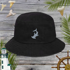 Black denim bucket hat with an embroidered grey hammerhead shark  logo on a wooden background with nautical elements.