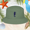 Green bucket hat with a seahorse design on a beach-themed background with starfish, sand, and palm leaves.