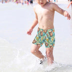 Child wearing colorful swim shorts with a parrot head pattern, standing in shallow water.